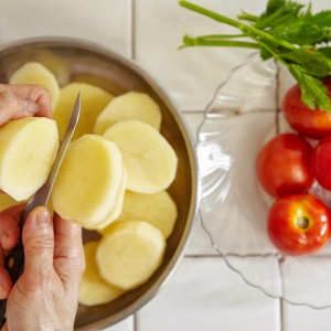 Cutting potato in big slice. Tomato and parsley on background